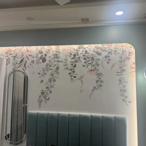 Bedhead wall shot upward from the pillow line: a teal channel-tufted headboard below a rounded-corner panel of trailing eucalyptus-and-blossom wallpaper