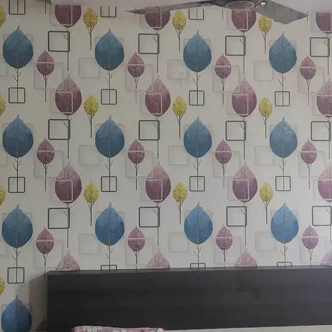 Bedroom accent wall covered in a colourful leaf-and-square print wallpaper behind a dark wood bed headboard, wardrobe to the left.