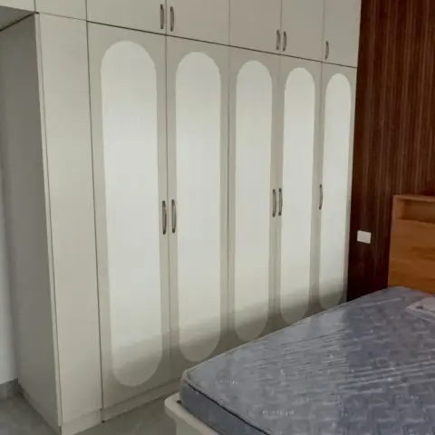 Bedroom at handover stage: a full-height cream wardrobe run whose five shutters each carry a tall arched fluted inlay