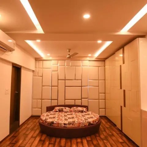Bedroom built around a circular brown platform bed, with an offset-block upholstered panel wall behind it