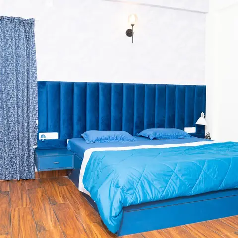 Bedroom built around one shade of blue: a wide navy velvet channel-tufted headboard running past the bed into a floating blue side drawer