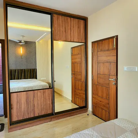 Bedroom corner showing a wood-and-mirror sliding-door wardrobe reflecting the bed, beside a wood-panelled internal door.