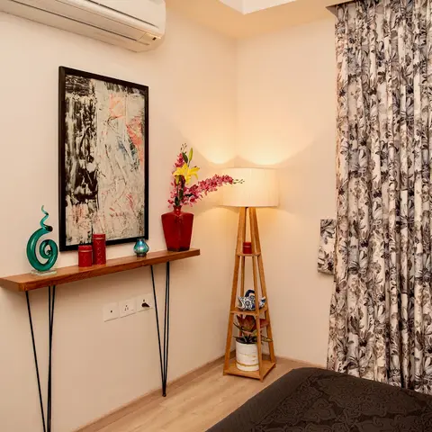 Bedroom corner styled with a live-edge wood console on black hairpin legs carrying a teal glass swirl sculpture and red pillar candles under a framed abstract