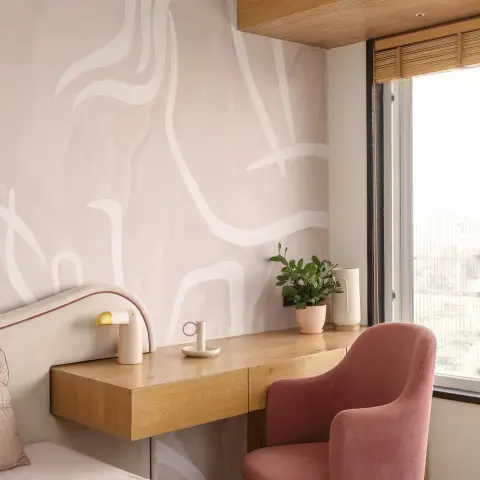 Bedroom corner where a floating oak ledge desk cantilevers off a blush wall painted with loose white brushstrokes
