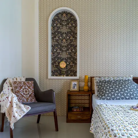 Bedroom corner where a leaf-motif beige wallpaper wall carries a tall white-edged arched recess papered in dark floral print with a small brass pendulum clock