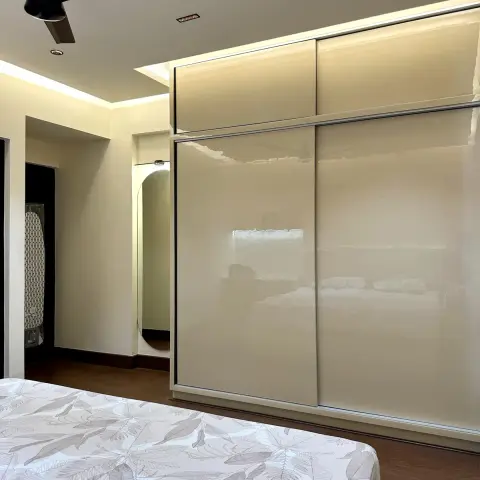Bedroom corner where an ivory high-gloss sliding wardrobe runs floor to loft beside an arch-topped full-height mirror recessed into the passage wall