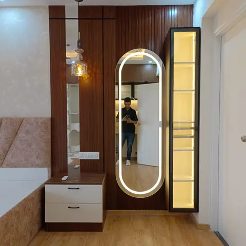 Bedroom corner with a capsule-shaped LED mirror mounted on fluted rosewood panelling, a slim black-framed display column lit warm yellow beside it