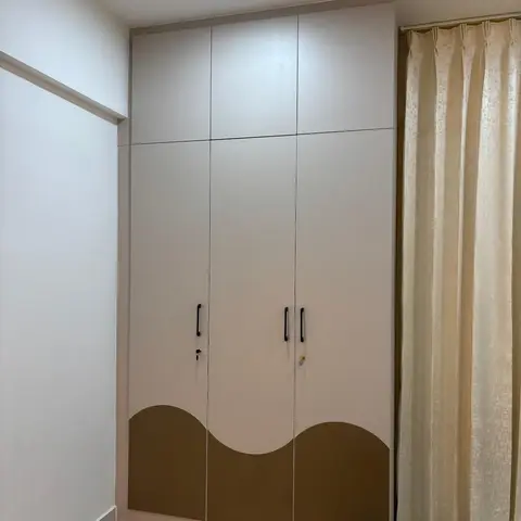 Bedroom corner with a floor-to-ceiling three-door wardrobe featuring a wave-pattern olive and cream laminate design
