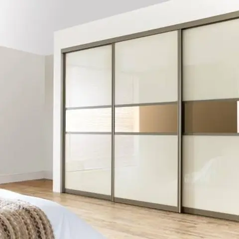 Bedroom corner with a fur throw over white bedding beside a three-panel sliding wardrobe with cream glass and bronze-mirror strip inserts.