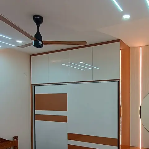 Bedroom corner with a white-and-tan sliding wardrobe under linear LED ceiling profiles, a carved wood bed edge in the foreground