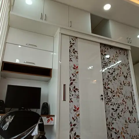 Bedroom corner with a white sliding wardrobe featuring floral leaf-pattern glass panels