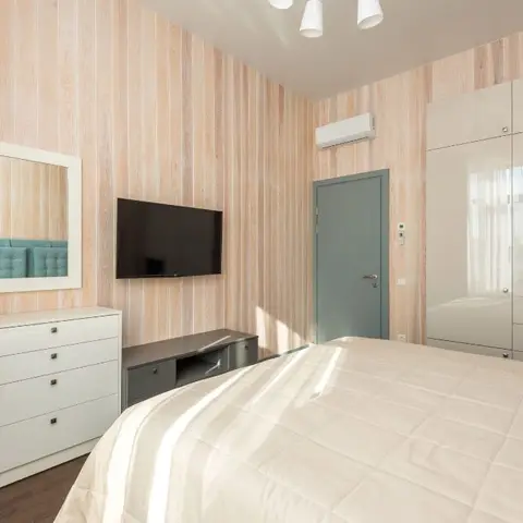 Bedroom lined floor-to-ceiling in whitewashed vertical pine planks, with a cream gloss wardrobe run, a wall-mounted TV