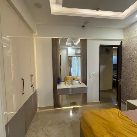Bedroom looking past a mustard-covered bed to a mirrored dressing niche flanked by dark fluted panels with concealed LED
