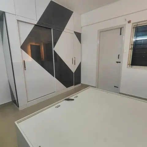Bedroom mid-fit-out with a white bed platform base (no mattress yet) and a bold black-and-white geometric-pattern sliding wardrobe.
