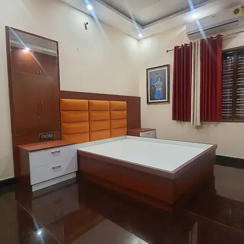 Bedroom mid-fitout with a padded orange-panel headboard, a mirrored wood dresser, and a bare bed base still awaiting its mattress.