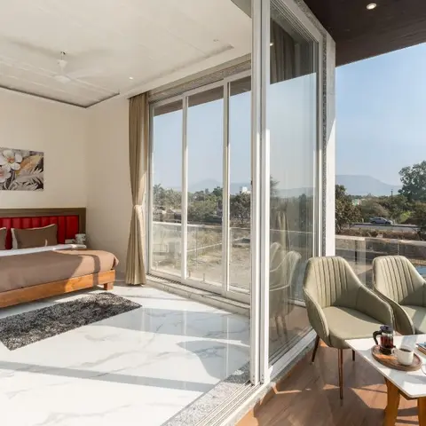 Bedroom opening through full-height sliding glazing onto a balcony with two olive channel-stitched armchairs