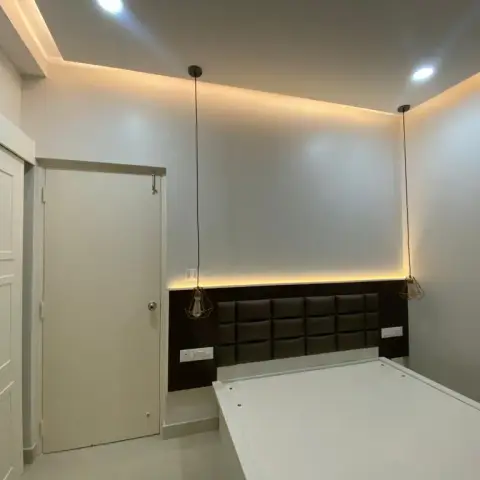 Bedroom photographed before handover - a bare white bed platform with no mattress against a dark leatherette grid headboard panel