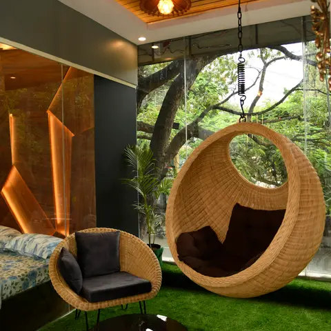 Bedroom's private balcony sit-out with a woven rattan hanging egg chair, matching armchair and glass-top rattan table on artificial turf