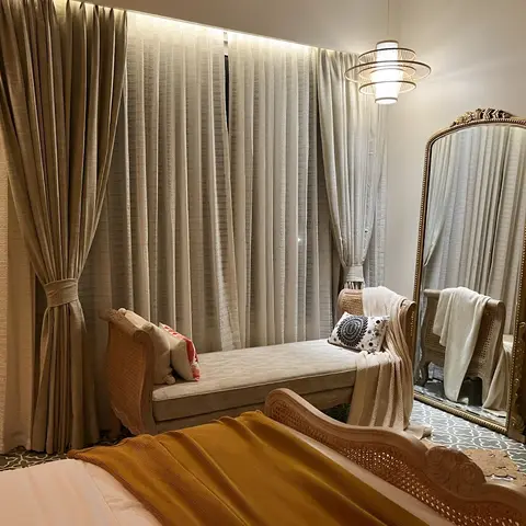 Bedroom seating nook with a rattan cane bench and armchair against floor-to-ceiling sheer drapery, a tall gilt-framed leaning mirror