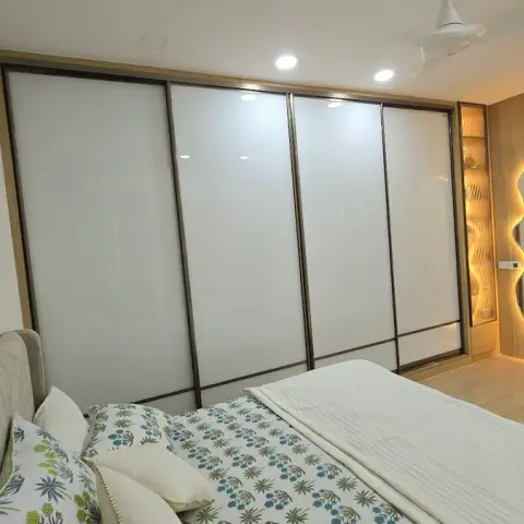 Bedroom seen across a printed bedspread and upholstered headboard towards a four-panel white lacquered-glass sliding wardrobe