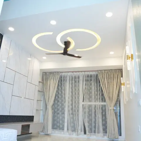 Bedroom shot upward from the corner of the bed, showing two interlocking illuminated rings in the false ceiling around a dark wooden fan
