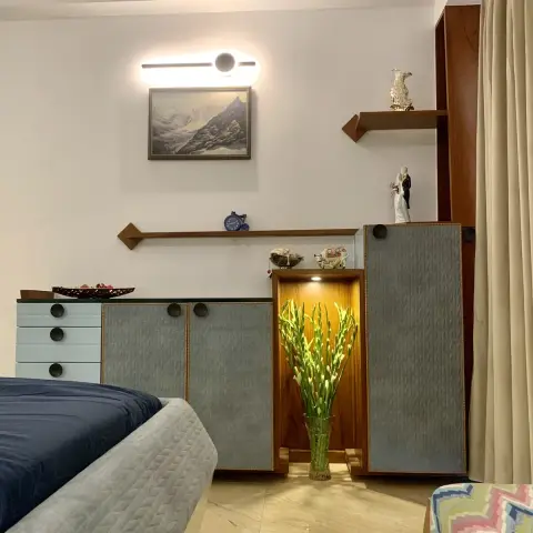 Bedroom storage run in grey textured shutters with teak lipping and round black knobs, a teak-lined niche lit over a vase of tuberoses