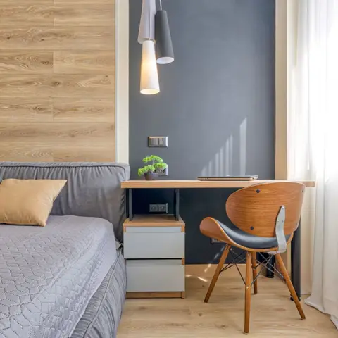 Bedroom study nook with a wood-panelled headboard wall, a black desk under a cluster pendant light, and a molded plywood chair by the window.