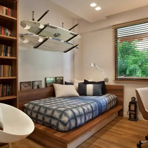 Bedroom-study with a double bed on a raised teak platform with drawer storage, surfboards racked on the wall above it
