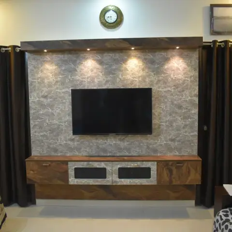 Bedroom TV wall clad in grey marble-look panel, washed by four spots set into a projecting walnut top box