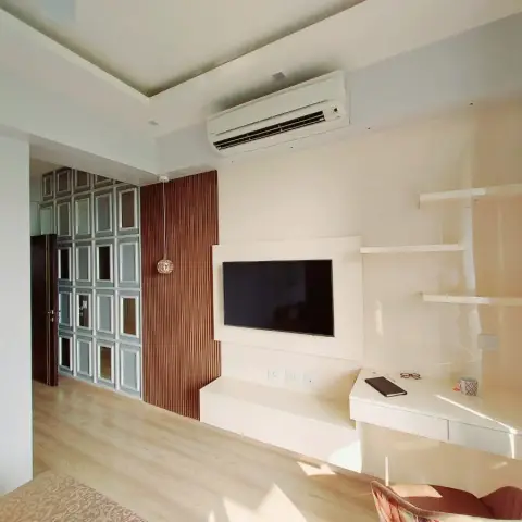 Bedroom TV wall with a fluted wood accent panel and pendant light beside a built-in study desk, with a mirrored wardrobe visible through the doorway.