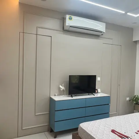 Bedroom TV wall with panel moulding either side of a wall-mounted AC, over a blue two-tone console holding a flatscreen.