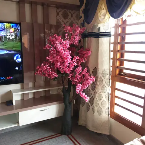 Bedroom TV wall with wood-slat panelling and damask wallpaper, styled with a large artificial pink-blossom tree in front of navy-and-cream pelmet curtains.