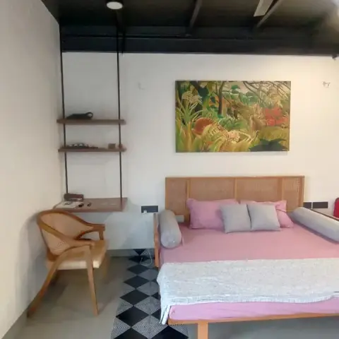 Bedroom under a blacked-out exposed-beam ceiling, with a cane-webbed headboard, pink bedding and a black-and-white diamond tile patch laid like a rug