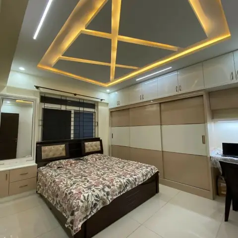 Bedroom under a diamond-shaped cove-lit POP ceiling, with a dark wenge storage bed facing a beige-and-cream sliding wardrobe run and a small desk with a