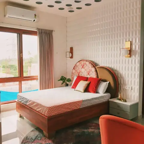 Bedroom under a polka-dot false ceiling of dark recessed circles, with a white 3D faceted tile wall behind a two-tone arched headboard in floral fabric