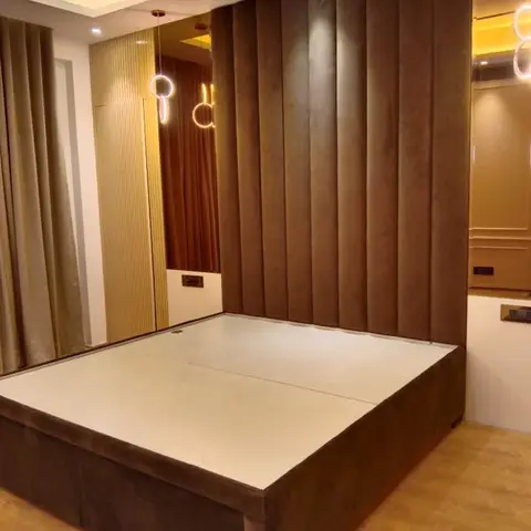Bedroom under finishing with a floor-to-ceiling channel-tufted velvet headboard wall, a fluted wood wardrobe reflected in the mirror, and ring pendant lights.
