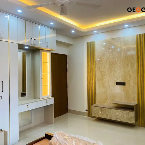 Bedroom under finishing with a white wardrobe and a lit dressing-mirror unit, and a marble-clad TV feature wall trimmed in gold fluted strips.