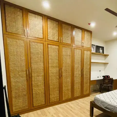 Bedroom wall filled floor-to-loft by a teak wardrobe with natural cane webbing set into every shutter and loft door