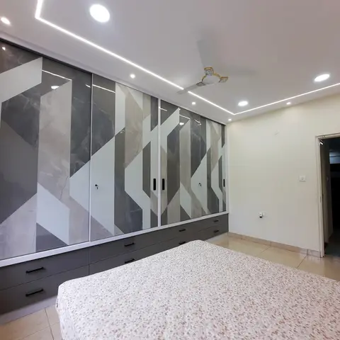 Bedroom wall taken up by a four-shutter sliding wardrobe in high-gloss grey-and-white marble-print laminate cut into diagonal blocks