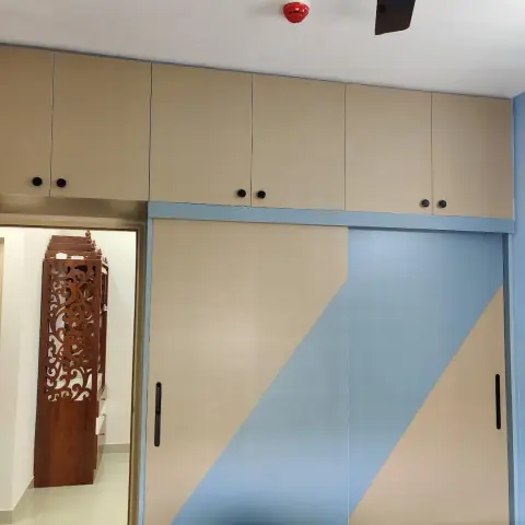 Bedroom wardrobe wall in beige laminate with a sky-blue diagonal band running across two sliding shutters and hinged loft units