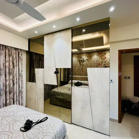 Bedroom wardrobe wall in bronze mirror and concrete-effect laminate cut on a diagonal, reflecting the bed and its floral wallpaper wall