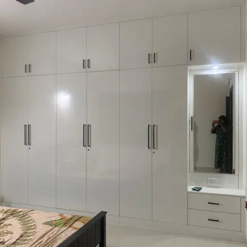 Bedroom wardrobe wall in glossy white laminate with a built-in mirrored dresser unit and drawers.