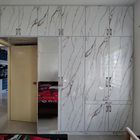 Bedroom wardrobe wall in white-and-gold marble-finish laminate with a full-height mirror door, opening onto the kitchen through a mustard-yellow door.