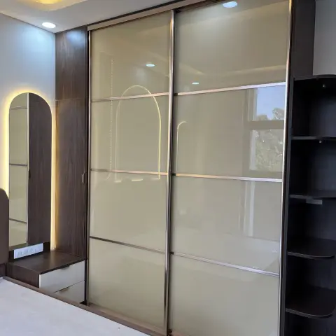 Bedroom wardrobe wall shot from the bed: cream lacquered-glass sliding shutters divided by rose-gold rails