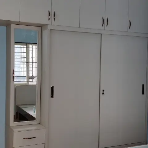 Bedroom wardrobe wall with a sliding-door wardrobe and overhead lofts beside a mirrored dressing unit with drawers, brown tile flooring.