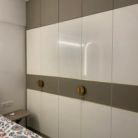 Bedroom wardrobe wall with alternating olive and glossy white laminate shutters, gold trim banding, and circular brass coin-style door pulls.
