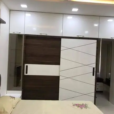 Bedroom wardrobe wall with dark wood and white sliding doors in a geometric diagonal-line pattern, flanked by mirrored overhead cabinets.