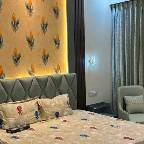 Bedroom where a backlit panel of gold feather-motif wallpaper glows above a sage diamond-tufted headboard, flanked by dark fluted panels