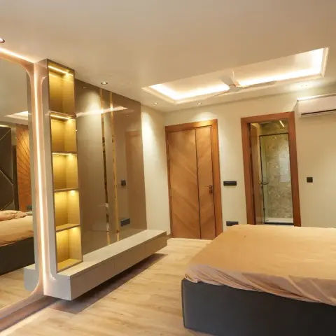 Bedroom where a rounded full-height LED-edged mirror and a backlit gold niche column form a half partition above a wall-hung drawer console