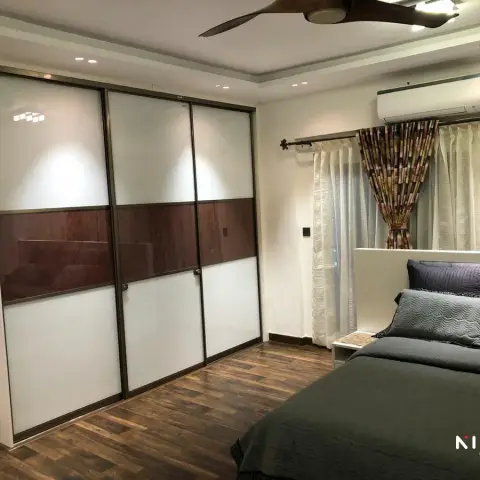 Bedroom where a three-shutter sliding wardrobe in white back-painted glass, banded across the middle in dark walnut